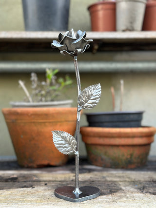 Handcrafted metal rose sculpture displayed on potting bench with terracotta pots