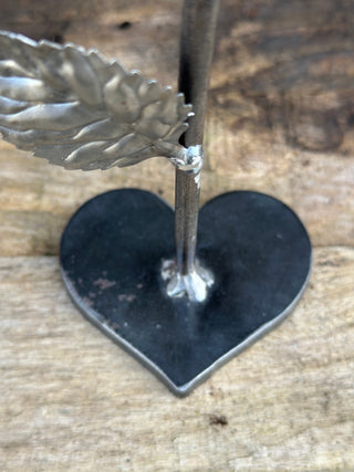 Steel rose ornament showing decorative heart shaped base and metal stem with leaf. 